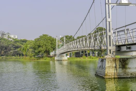 Small wooden bridge and walking lane. Small metal white footbridge over narrow canal in the park (Kolkata, Rabindra Sarovar Lake, India)