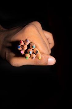 Human hand close up of a young artist holding showing colorful office sketch pencils in isolated black background with copy space. Childhood education, drawing writing, design and creativity concept.