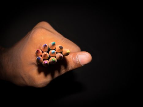 Human hand close up of a young artist holding showing colorful office sketch pencils in isolated black background with copy space. Childhood education, drawing writing, design and creativity concept.