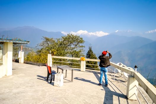 A man taking a photographs of Kanchenjunga mountain from Pelling helipad, Sikkim India on a sunny summer day during christmastime. Travel vacation concept.