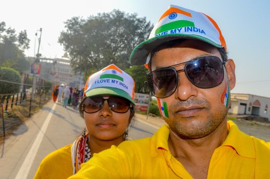 Selective focus on man. Cricket fans with painted face in Indian tricolor. Happy young loving couple looking at camera. Capturing bright cheerful moments taking Selfie on camera and standing outdoors.