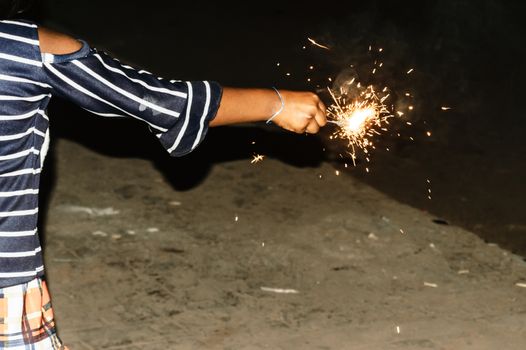 Sparklers on hand on black background on a low light evening. Selective focus on sparklers. Mother, Daughter, Woman, Lady, girl, kid, child holding sparkles.