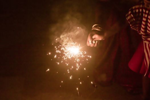 Sparklers on hand on black background on a low light evening. Selective focus on sparklers. Mother, Daughter, Woman, Lady, girl, kid, child holding sparkles.