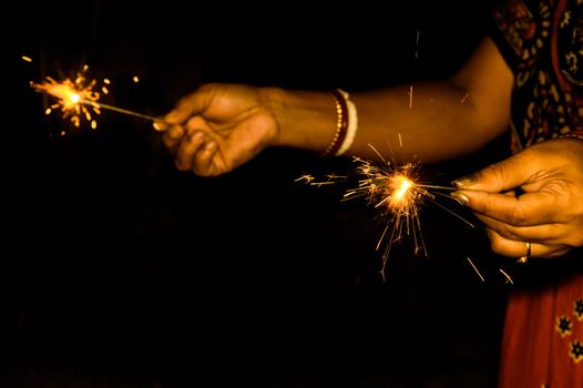 Sparklers on hand on black background on a low light evening. Selective focus on sparklers. Mother, Daughter, Woman, Lady, girl, kid, child holding sparkles.