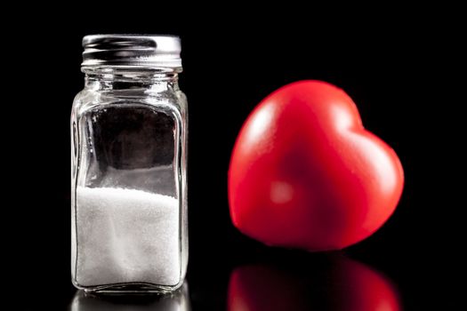 Heart and salt isolated on black background with reflection