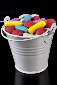 Colored pills medicine in a white bucket isolated on black background