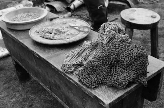 Chain mail display at a Medieval Fair. A pile of armour lies on a wooden bench with tools and metal rings under construction - monochrome processing