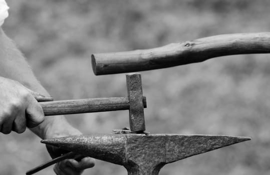 Close-up of man's hand using a rustic hammer to work a piece of metal on an anvil at a Medieval Fair - monochrome processing