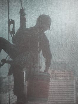 Silhouette images and shoot through transperent curtain effect from inside building which a man cleaning the window of high office building with his equipment such as wipe, sponge, bucket and high risk of danger