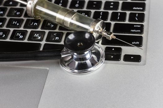 Black Stethoscope Closeup and Glass Syringe On Silver Laptop  With White Background