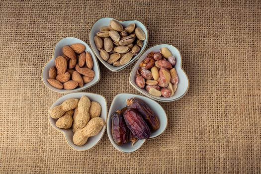 Peanuts, almonds, dates and pistachio  in heart shaped plates on canvas