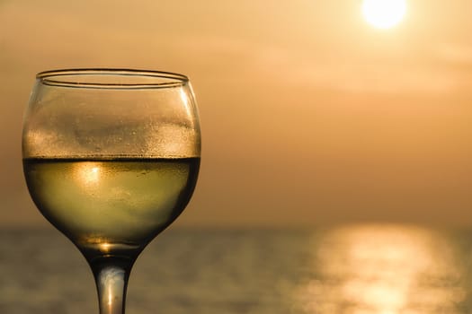 A side angle view shot of a glass of white wine against the Ionian Sea during the sunset.
