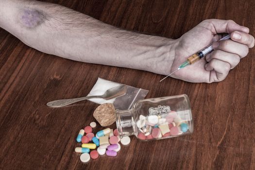 Bruised hand with needle and pills on the table

