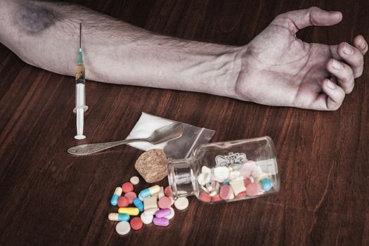 Bruised hand with needle and pills on the table