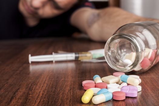 Bruised hand with needle and pills on the table