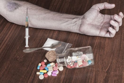 Bruised hand with needle and pills on the table
