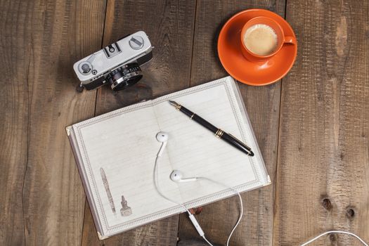Headphones on empty notebook with coffee on wood table with old camera