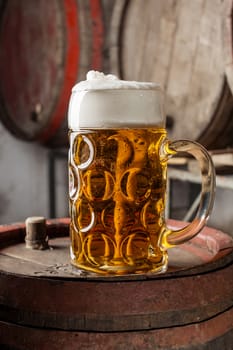 Beer in glass with foam on old wood barrel with other barrels in the background