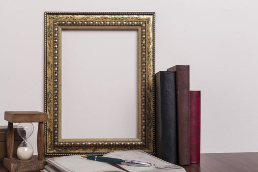 Golden portrait frame with books and horglass on wood table