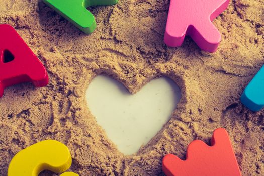 Heart shape and colorful Letters made of wood on sand