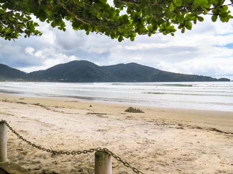 View of beach in sunny day with waves and sand castle.