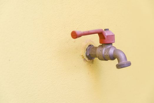 Red faucet on a yellow wall background.