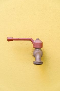 Red faucet on a yellow wall background.
