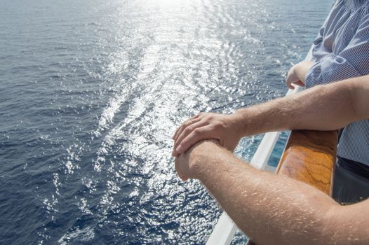 The concept of sea cruises. Men's hands on the railing of the cruise ship on the background of the sea waves and sunset.
