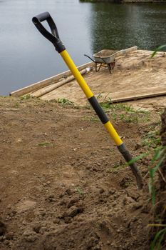 Wheelbarrow and shovel for construction in site building area at the river. Construction wheelbarrow and shovel in the sand by the river Daugava, Latvia.