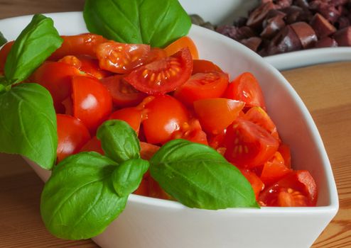white ceramic cup with chopped fresh tomatoes and basil, sliced ​​black olives on the background