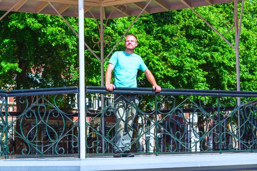 Young man stands in a gazebo and looks into the distance