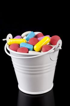 Colored pills medicine in a white bucket isolated on black background