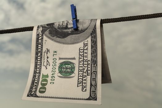 One hundred american dollar drying on string with cloudy  sky