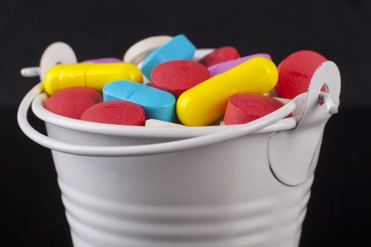 Colored pills medicine in a white bucket isolated on black background