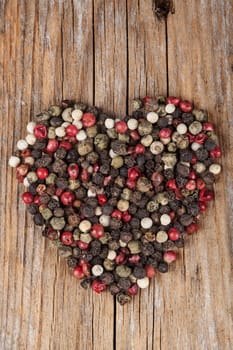 Color pepper mixed spices heart shaped  on old wood background