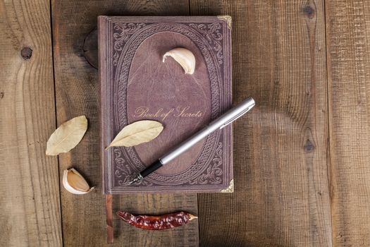 Book of Secrets brown closed cookbook on old wood background with spices