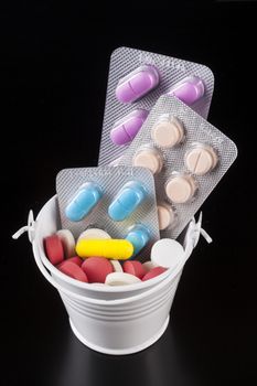 Coloerd pills medicine in a white bucket isolated on black background