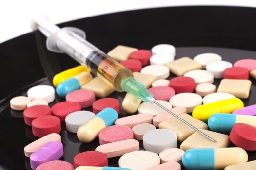 syringe on colored pills in black plate