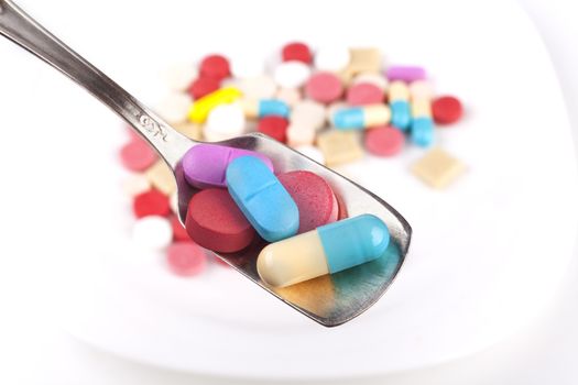 Silver spoon full with  medicine and colored pills in the background