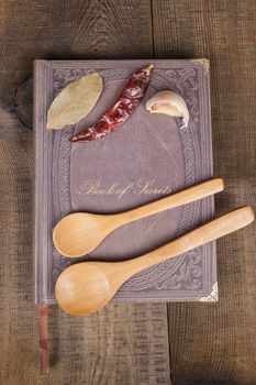 Book of Secrets brown closed cookbook on old wood background with spices and two  spoons