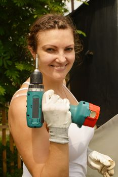 Young beautiful woman in a white t-shirt, holding a screwdriver with gloves. Woman Builder posing outdoors.