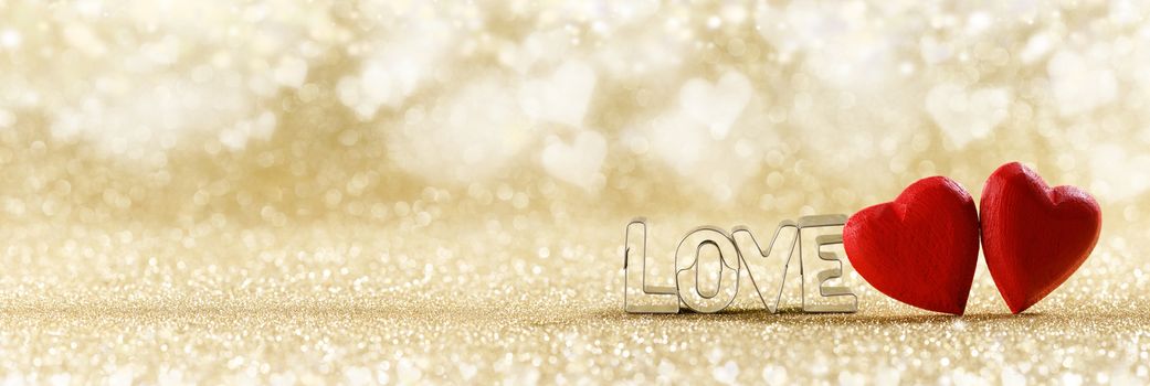 Two red handmade wooden hearts and word love on golden bright glitter lights bokeh background