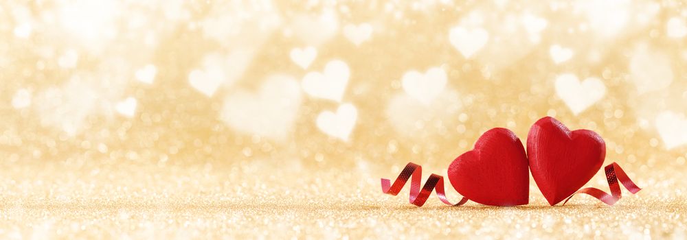 Two red handmade wooden hearts and ribbons on golden bright glitter lights bokeh background