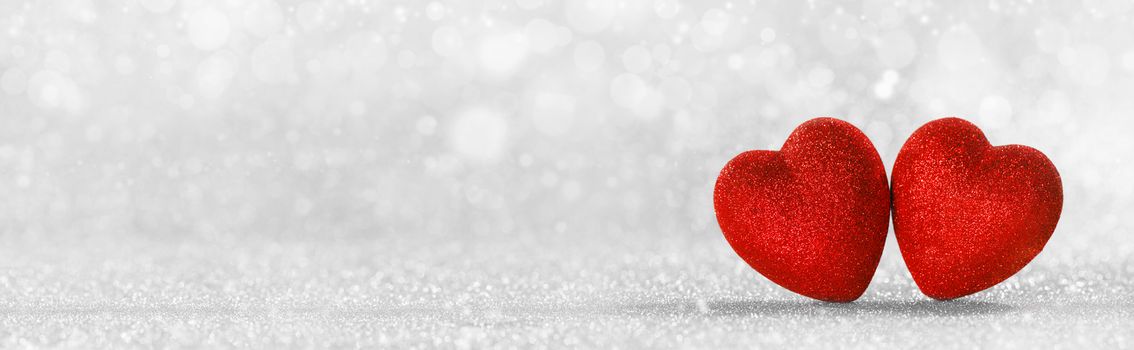Two red handmade wooden hearts on silver bright glitter lights bokeh background