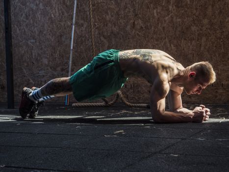 Attractive blond young man shirtless in gym working out, doing exercises for abs.