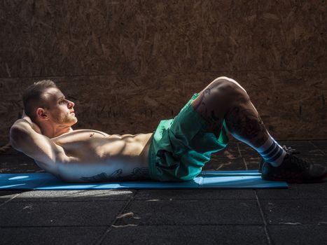 Attractive blond young man shirtless in gym working out, doing exercises for abs.