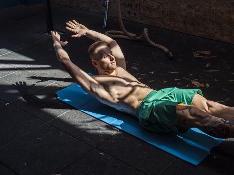 Attractive blond young man shirtless in gym working out, doing exercises for abs.