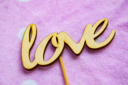 The word love is made of wooden letters on a pink background with white peas. Valentine's day concept, top view.