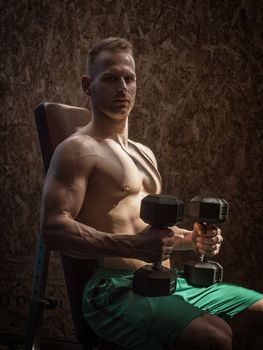 Handsome muscular young man exercising biceps in gym with dumbbells.