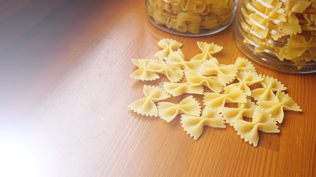 Pasta in the form of bows scattered from glass jar. Italian handmade pasta on the wooden background.